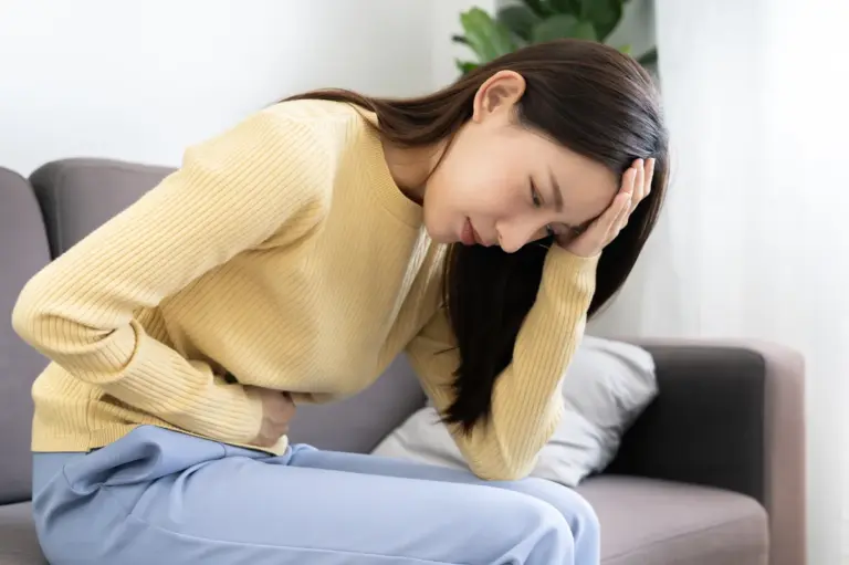 A woman sitting on a sofa leaning forward holding her stomach and her head