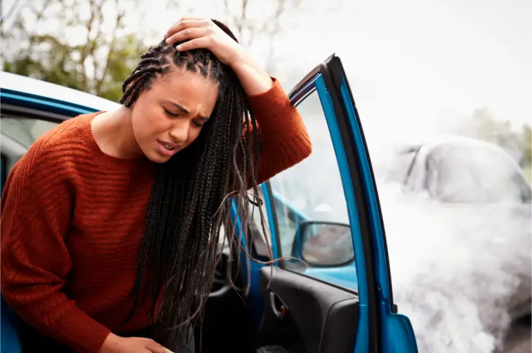 Driver holding her head in pain beside her car after a collision
