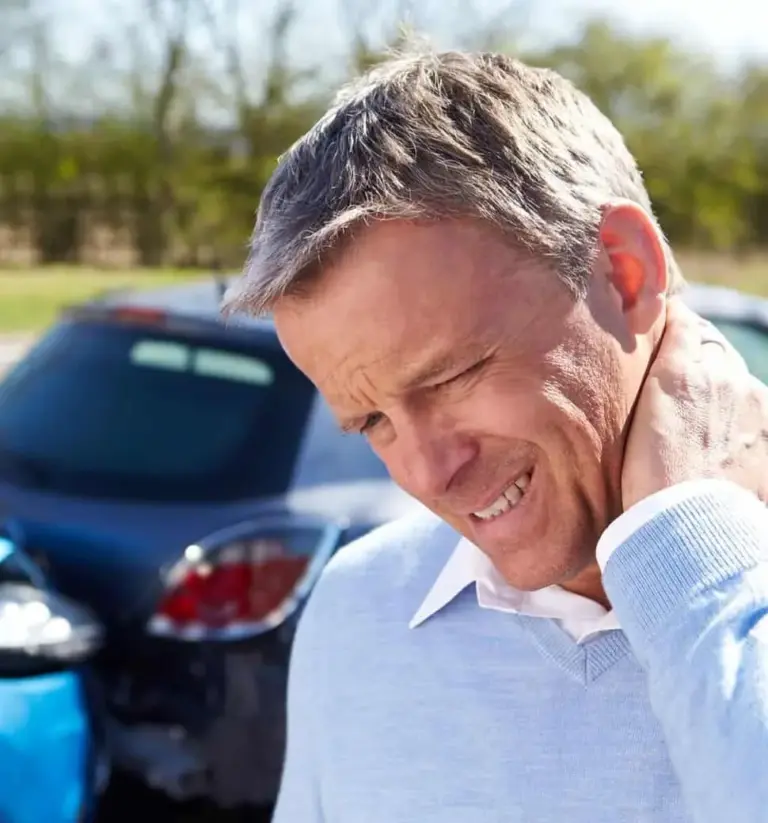 A man holding his neck in pain standing in front of two collided cars