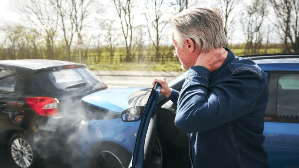 A person seated in a car holding their neck after a collision