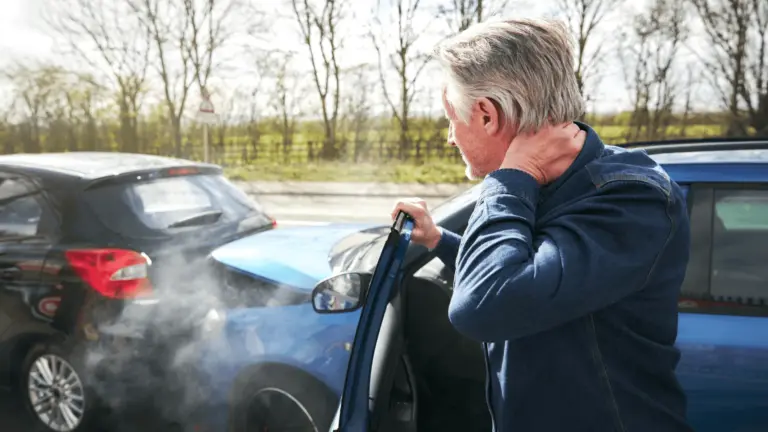 A person seated in a car holding their neck after a collision