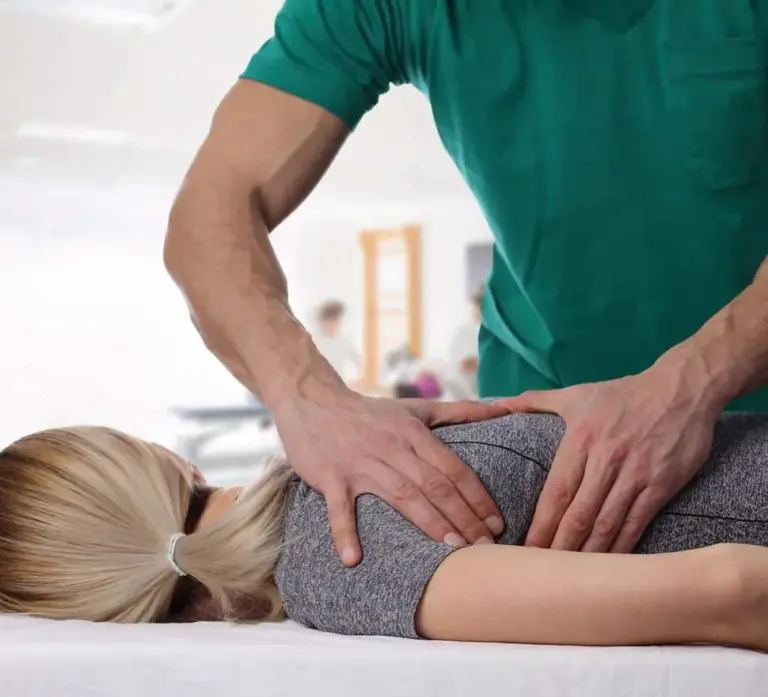 A chiropractor applying pressure to the lower back of a patient lying face down on a treatment table