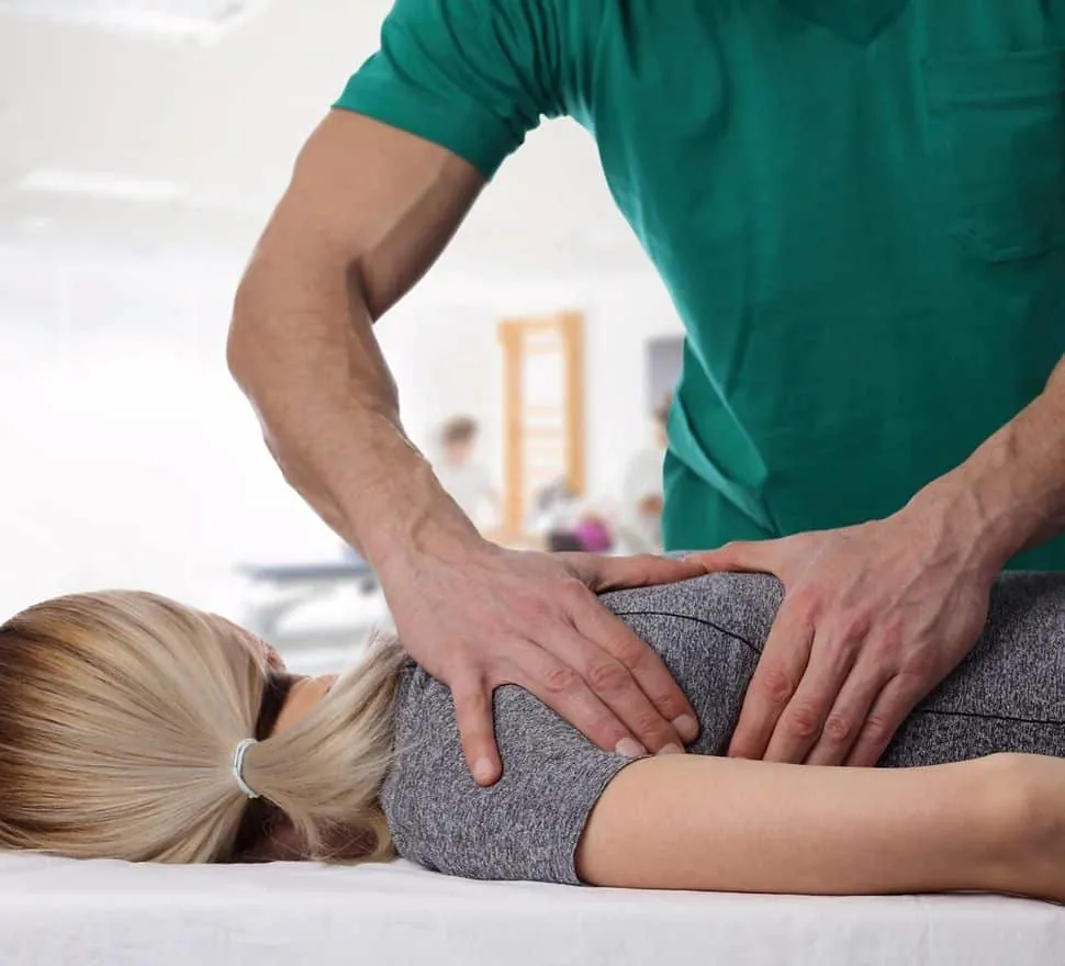 A chiropractor applying pressure to the lower back of a patient lying face down on a treatment table