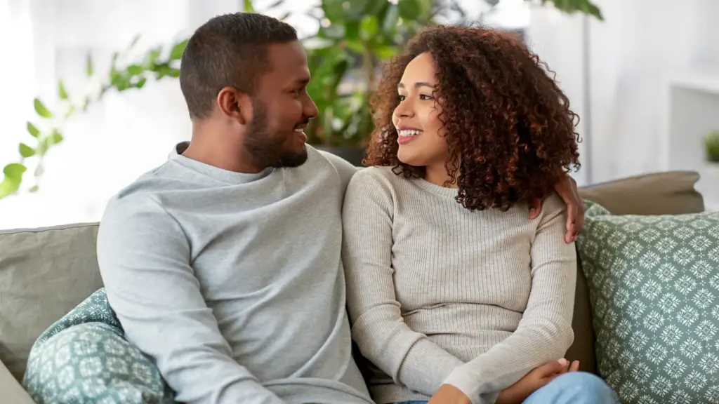 Couple sitting together on a sofa, turned towards each other and smiling