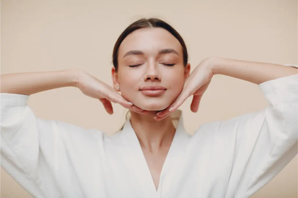 Woman in a white robe framing her face with her hands after a facial treatment