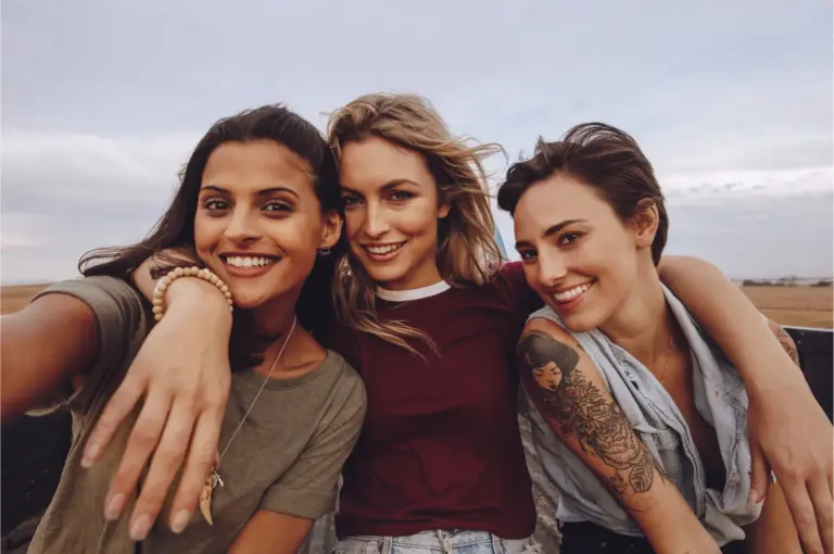 Three friends standing arm in arm and smiling outdoors