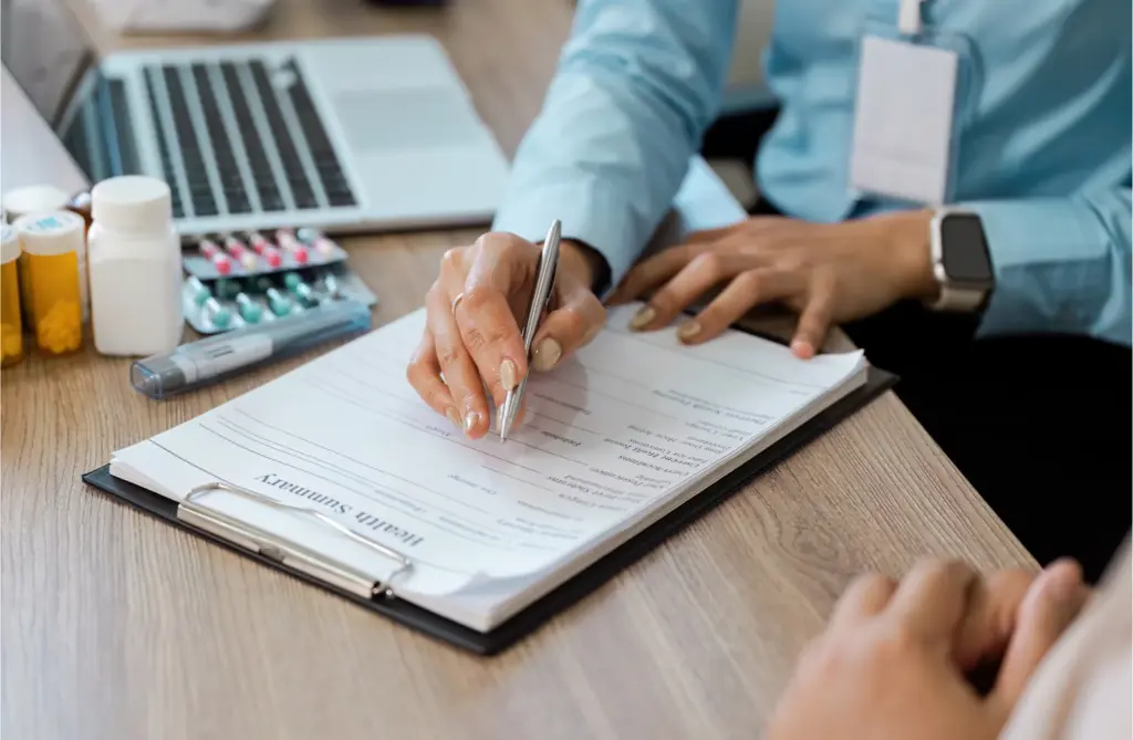 Clinician completing a health summary form beside prescription bottles