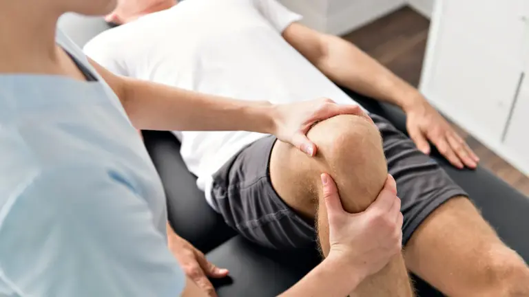 A clinician supporting a patient bent knee during a joint examination on a treatment table