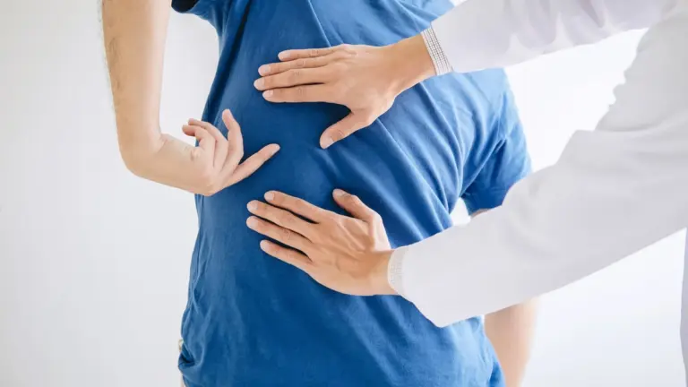 A clinician placing both hands on a patient lower back during an examination