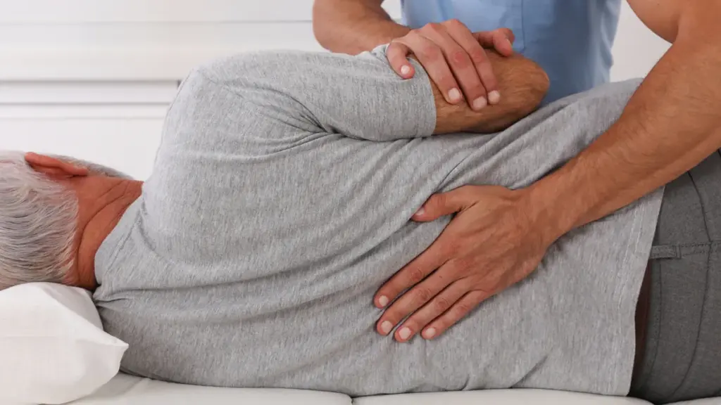 A chiropractor performing a side-lying lower back adjustment on an older patient