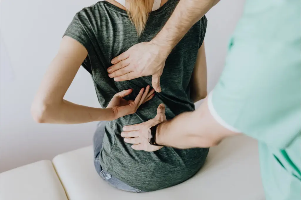 Clinician palpating the lower back of a seated patient with both hands