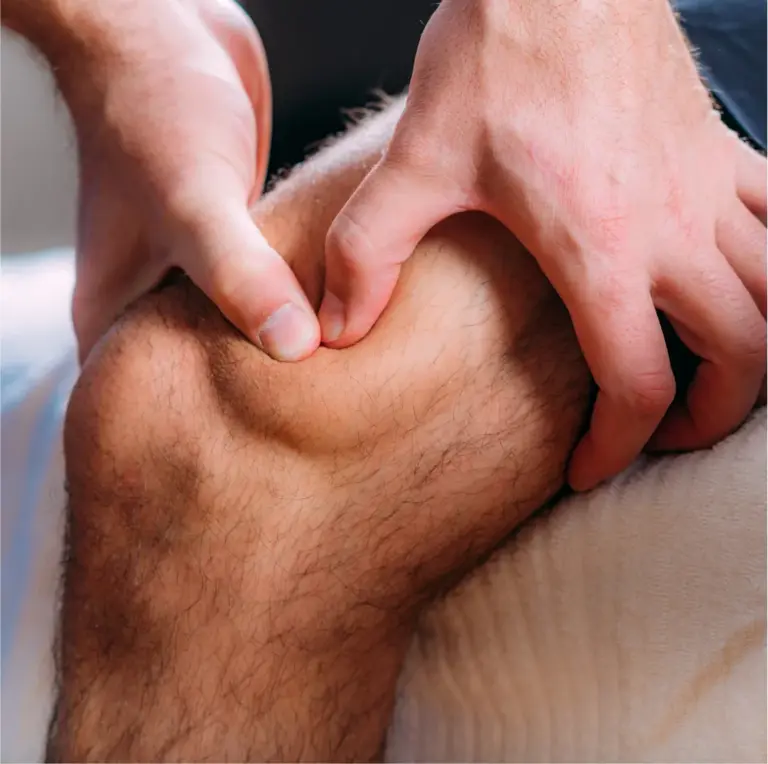 Therapist's hands applying pressure to the muscles above a patient's knee
