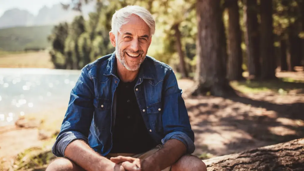 Man with white hair sitting outdoors beside a lake