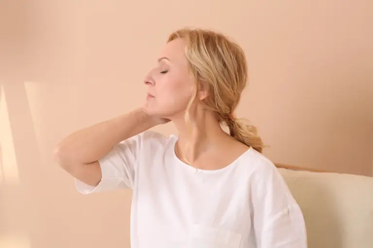 Woman sitting on a sofa holding the side of her neck in pain
