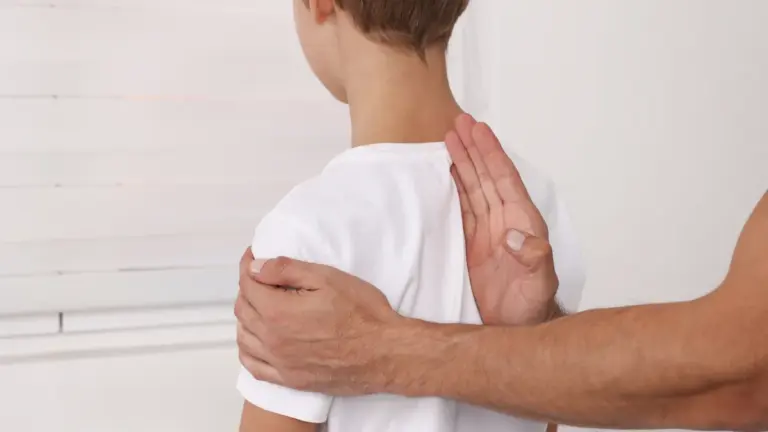 A clinician resting a hand on a child upper back during an examination