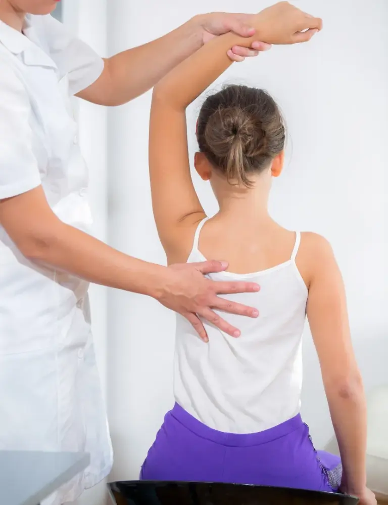A clinician raising a girl arm while supporting her back during an assessment