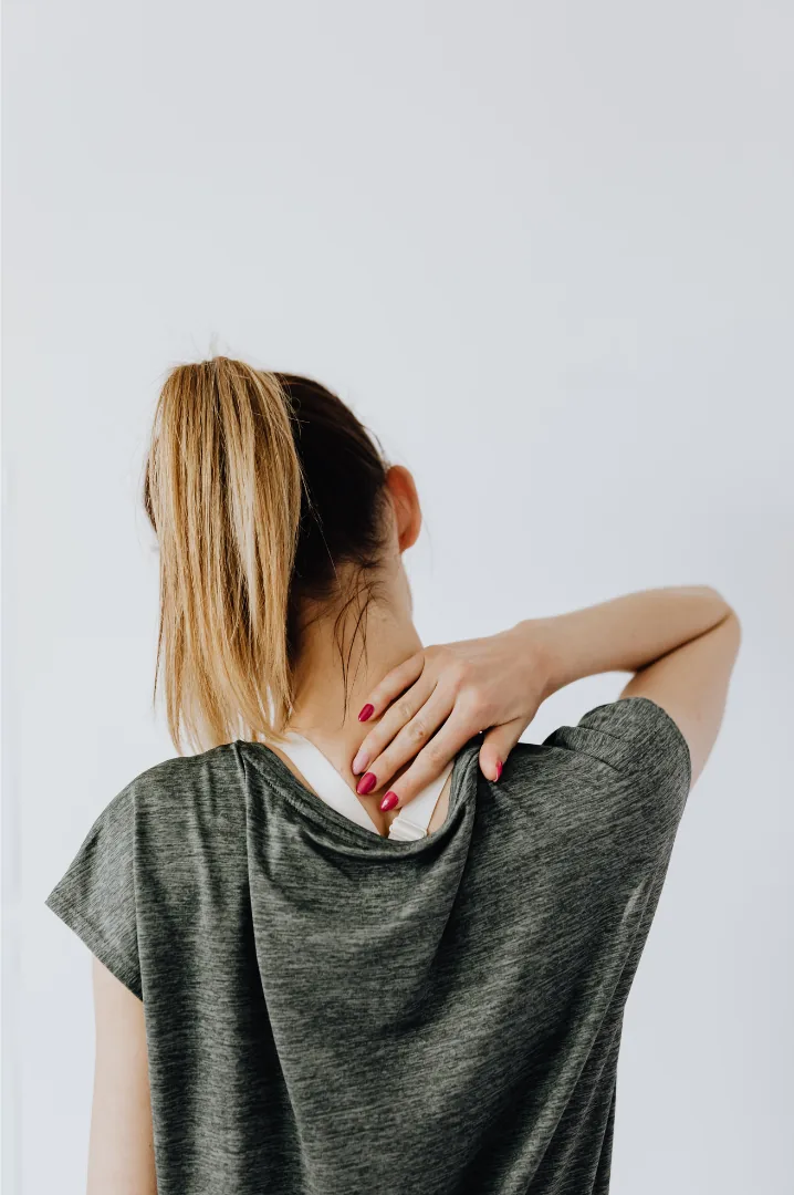 A woman seen from behind reaching over her shoulder to her upper back