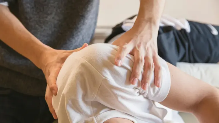 A clinician pressing on a patient knee with both hands during treatment on a table