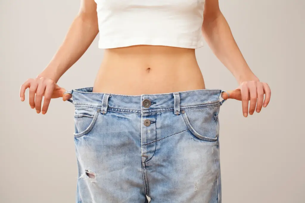 Person holding out the waistband of a pair of jeans that are now too large
