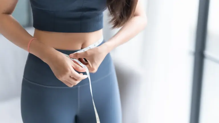Woman in workout clothes measuring her waist with a tape measure