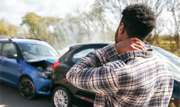 Man holding his neck at the roadside in front of two collided cars